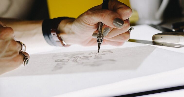 person lettering on tracing paper using mechanical pencil